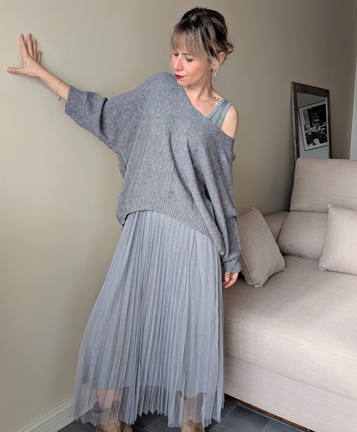 Vestido gris de falda plisada combinado con jersey de punto con un hombro descubierto.