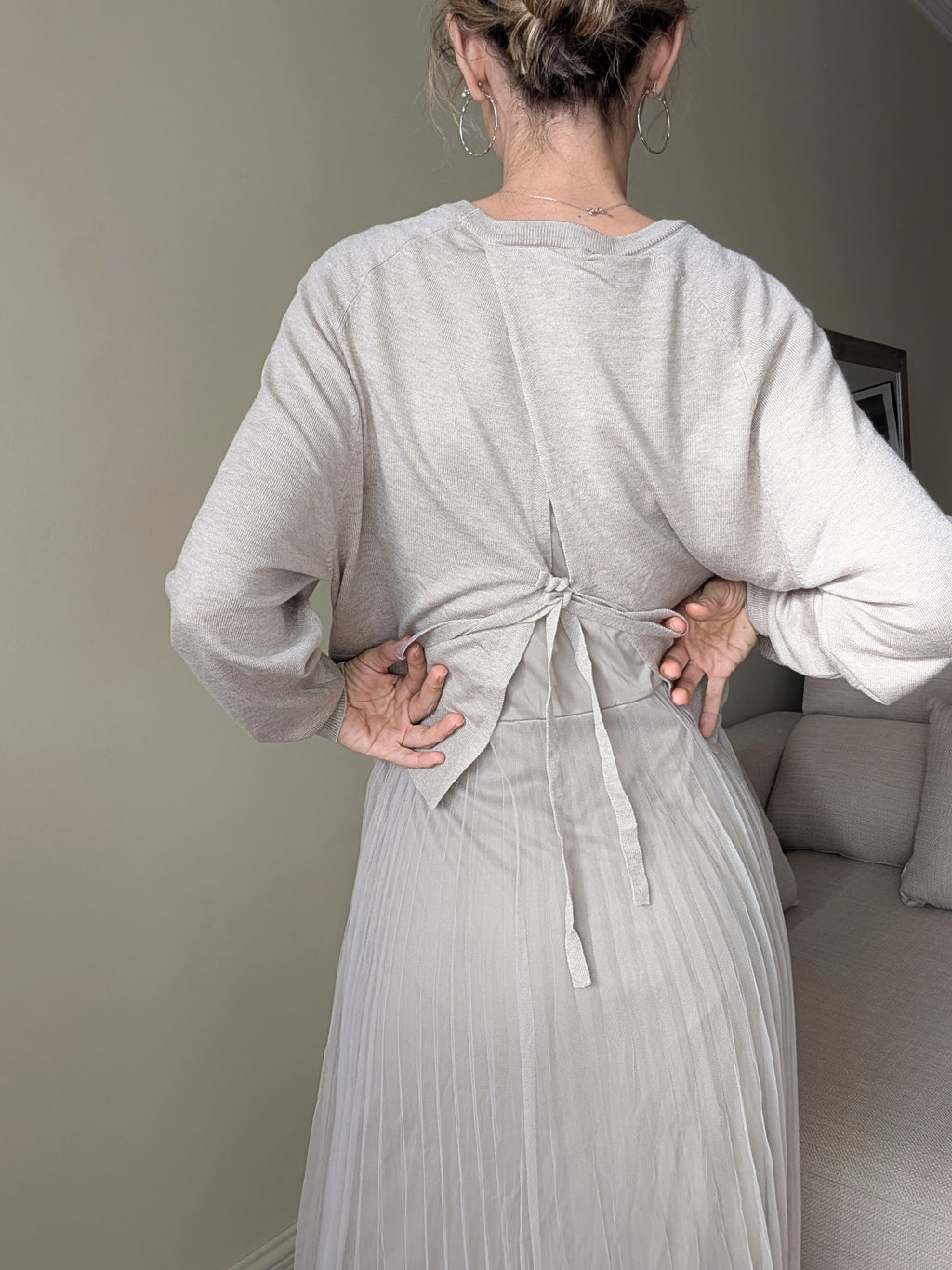 Espalda del jersey beige con cintas anudadas sobre el vestido plisado.