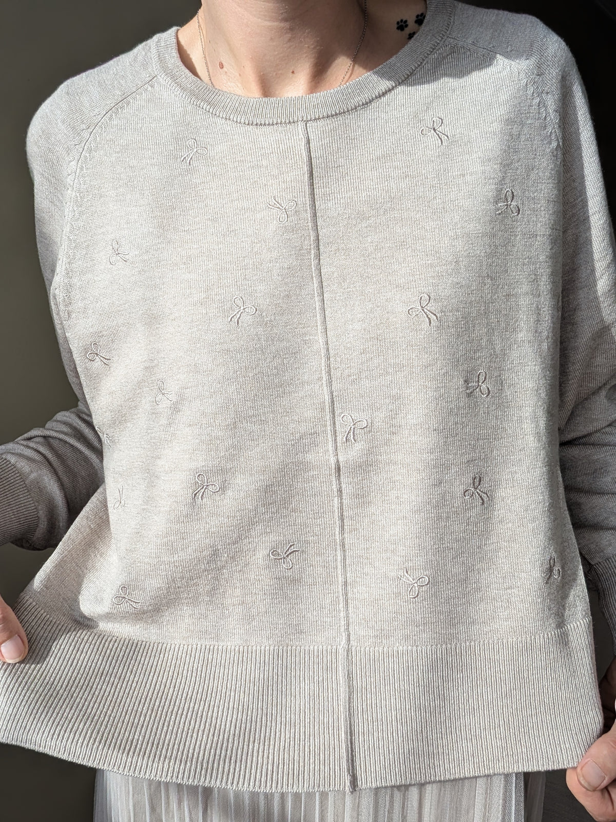 Detalle del cuello redondo y pequeños lazos bordados del jersey beige.