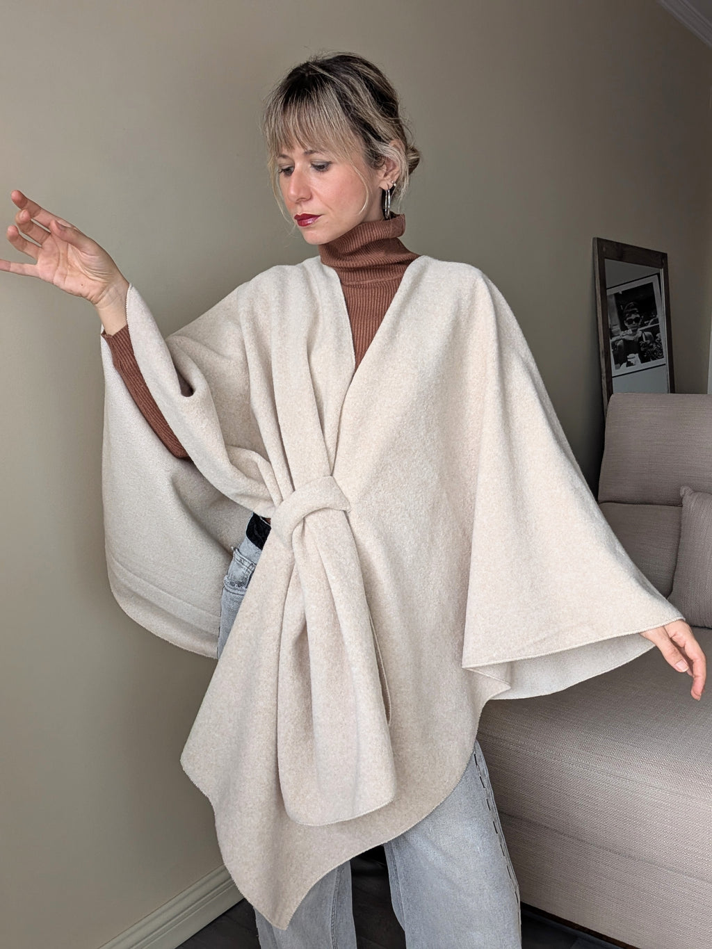 Capa beige de corte amplio con brazos extendidos y caída asimétrica.