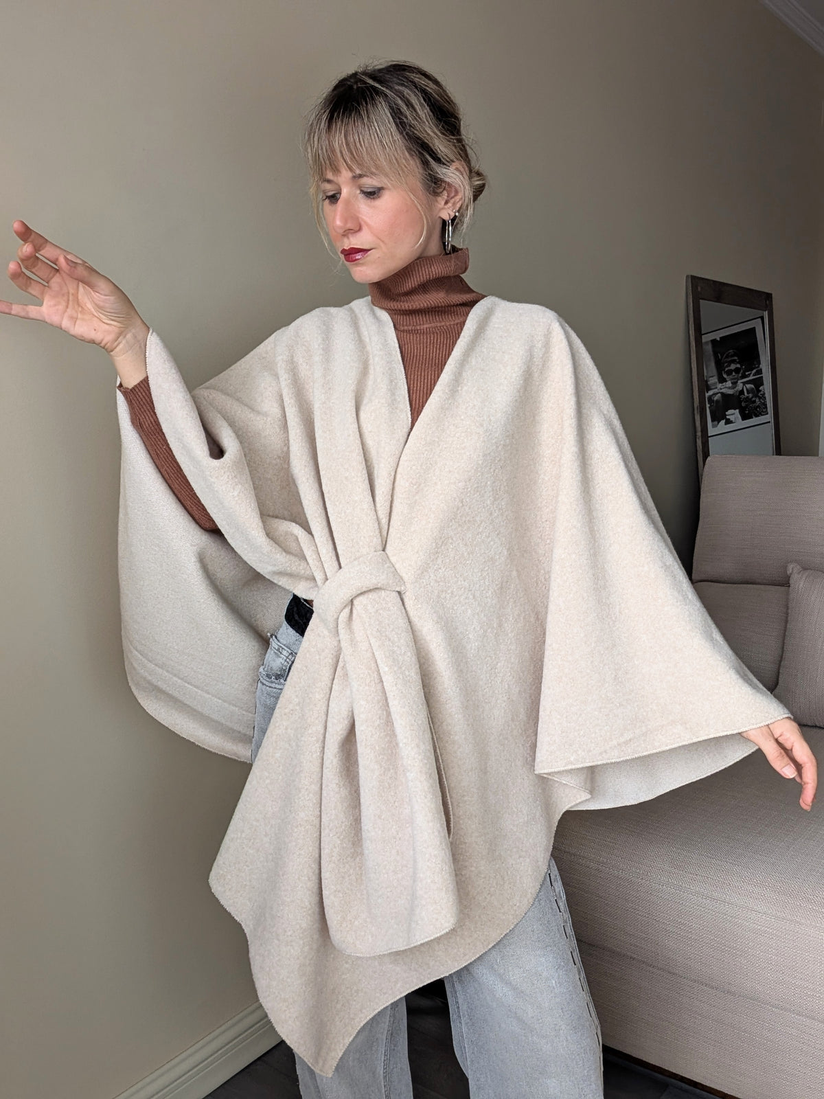 Capa beige de corte amplio con brazos extendidos y caída asimétrica.